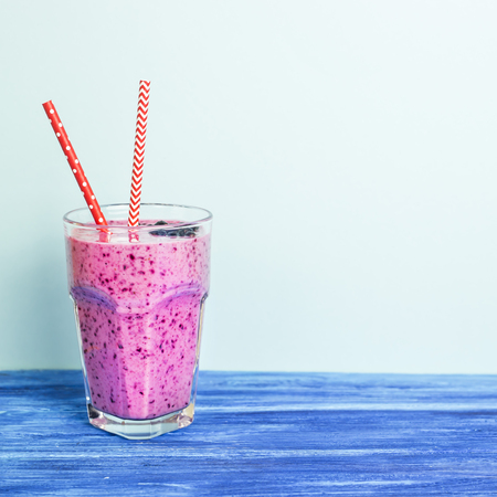 Banana currant smoothies of violet color with red straws stand on a wooden table on a blue background. Background, copyspaceの写真素材