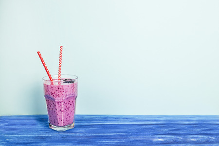 Banana currant smoothies of violet color with red straws stand on a wooden table on a blue background. Background, copyspaceの写真素材