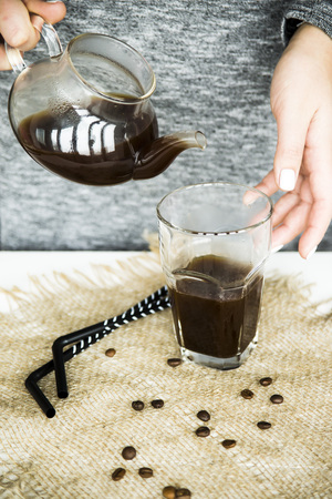 A girl in a gray dress pours coffee into a large glass to prepare a summer cooling coffee drinkの写真素材