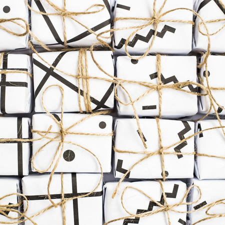 Small gift boxes of white color with black geometric patterns tied with twine. On a white background. Top view, flat layの写真素材