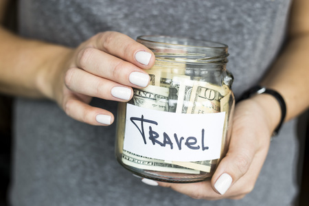 A woman is holding a piggy bank for travel full of dollars. Accumulation of finance conceptの写真素材