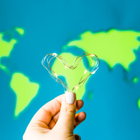 Heart of a garland with lights in a woman's hand against a background of a bright world map. Love of...