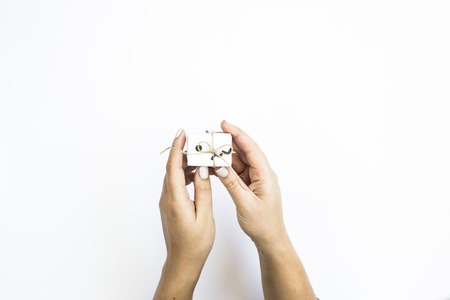 Female hands hold a small white gift in a minimalist style. On a white background. Flat lay, top viewの写真素材