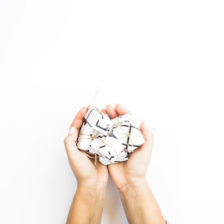 Female hands hold small white small gifts in minimalist style. On a white background. Flat lay, top...