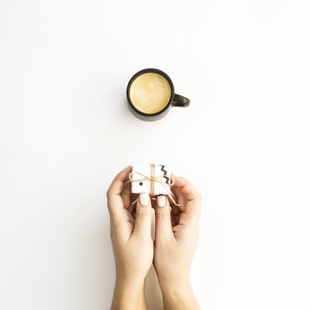 Female hands holding a small minimalist gift near a cup of coffee on a white background. Flat lay, top viewの写真素材