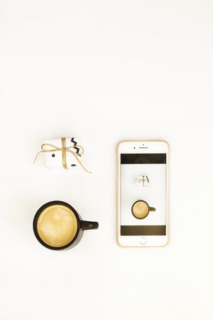 A cup of coffee, a small minimalist gift and a smartphone on a white background. Photos for social networks concept. Flat lay, top viewの写真素材