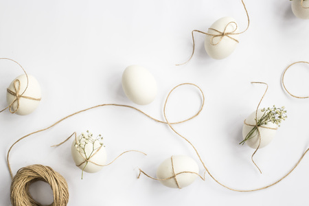 Easter eggs are minimalistically decorated with twine and gypsophila flowers. On a white background with a brown rope. Top view, flat layの写真素材