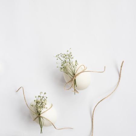 Easter eggs are minimalistically decorated with twine and gypsophila flowers. On a white background with a brown rope. Top view, flat lay. Copyspaceの写真素材