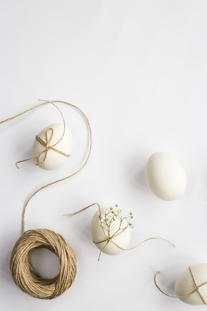 Easter eggs are minimalistically decorated with twine and gypsophila flowers. On a white background with a brown rope. Top view, flat lay. Copyspaceの写真素材