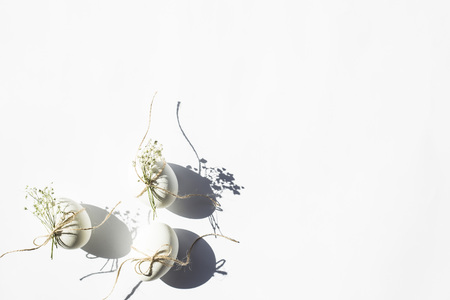White minimalistic Easter eggs decorated with twine and flowers of gypsophila on a white background in bright light with deep shadows. Easter concept. Top view, flat layの写真素材