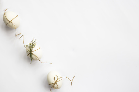 White minimalistic Easter eggs decorated with twine and flowers of gypsophila on a white background lined with a line. Easter concept. Top view, flat layの写真素材