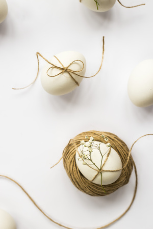 Easter eggs are minimalistically decorated with twine and gypsophila flowers. On a white background with a brown rope. Top view, flat layの写真素材