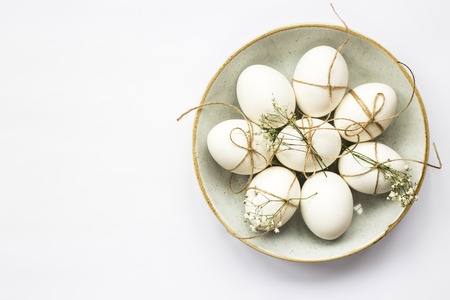 Easter eggs are minimalistically decorated with twine and gypsophila flowers in a blue round plate on a white background. Top view, flat lay. Copyspaceの写真素材