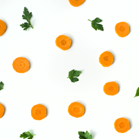 Bright round ringlets of carrots and green twigs of parsley on a white background. Healthy food concept. Top view, flat layの写真素材