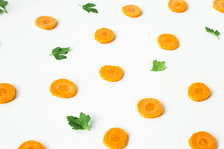 Bright round ringlets of carrots and green twigs of parsley on a white background. Healthy food concept. Top view, flat layの写真素材