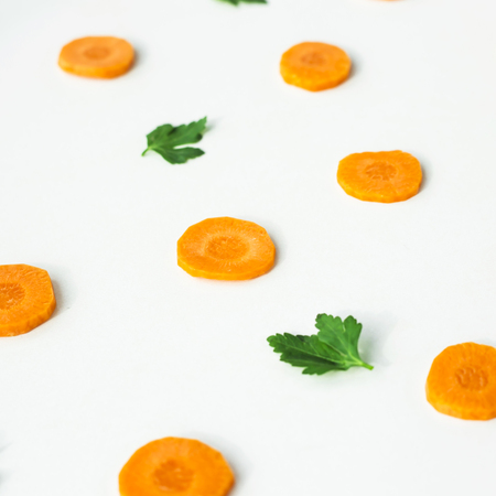 Bright round ringlets of carrots and green twigs of parsley on a white background. Healthy food concept. Top view, flat layの写真素材
