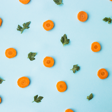 Bright round ringlets of carrots with green parsley sprigs on a blue background. Top view, flat layの写真素材