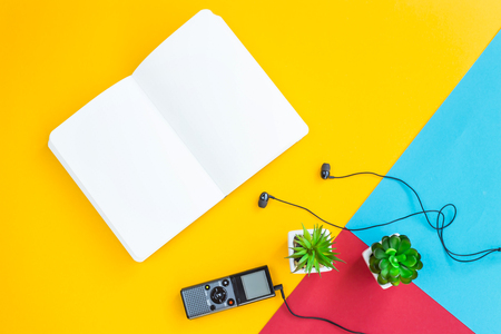 Dictaphone with headphones next to green succulents and white notebook. Workplace of a journalist, writer. On a bright combined background. Top view, flat layの写真素材