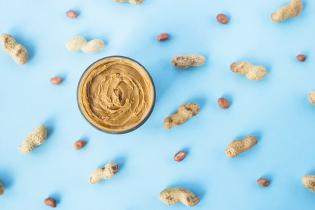 A jar of hazelnut paste among peanuts in shell and without on a blue background. Vegan product. American breakfast. Top view, Flat layの写真素材