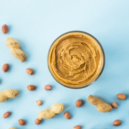 A jar of hazelnut paste among peanuts in shell and without on a blue background. Vegan product. American breakfast. Top view, Flat layの写真素材