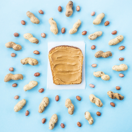 Bread toast with walnut paste among peanuts in shell and without on a blue background. Bright vegan food concept. Top view, Flat layの写真素材