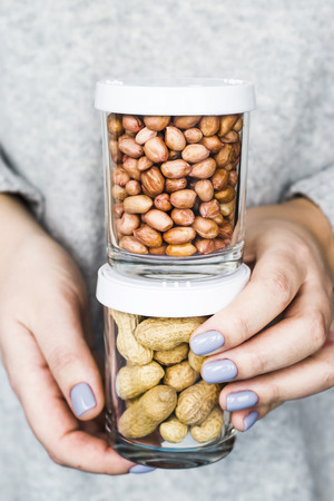 The woman holds in her hands two jars - with peanut in the shell and peeled peanuts. Vegan and natural food conceptの写真素材