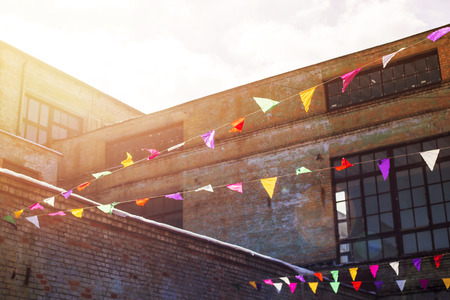 Multicolored triangular decorative flags hang on the background of old loft brick buildings with large windows in sunlight. Backgroundの写真素材