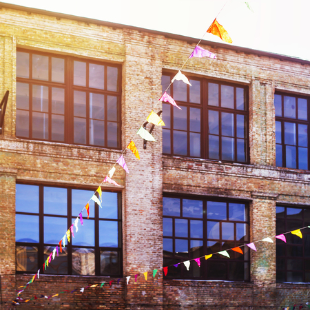 Multicolored triangular decorative flags hang on the background of old loft brick buildings with large windows in sunlight. Backgroundの写真素材