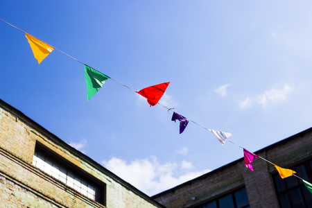 Multi-colored flags decoration hanging on a background of old buildibg and blue sky with white clouds. Copyspaceの写真素材