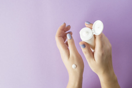Female hands with a blue manicure hold a hand cream. Female hand care. Beauty and care procedures conceptの写真素材