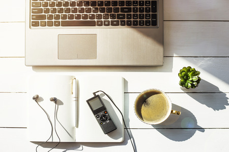 Dictaphone with headphones on a light worktable of a journalist with a notebook, a green succulent and a laptop. In the sunlightの写真素材