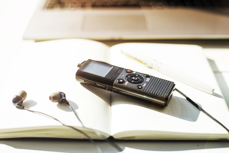 Dictaphone with headphones on a light worktable of a journalist with a notebook, a green succulent and a laptop. In the sunlightの写真素材
