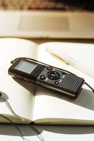 Dictaphone with headphones on a light worktable of a journalist with a notebook, a green succulent and a laptop. In the sunlightの写真素材