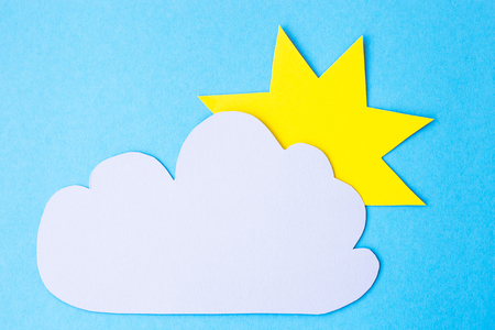 Yellow paper sun next to a gray cloud on a blue background. Cloudy weather conceptの写真素材
