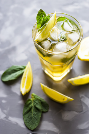 A glass glass with a cold tea with ice, mint and lemon on a gray concrete background. Summer cooling drinkの写真素材