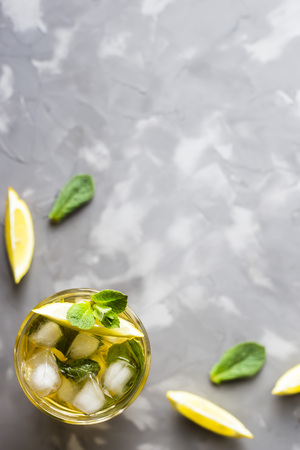 A glass glass with a cold tea with ice, mint and lemon on a gray concrete background. Summer cooling drink. Copyspace. Top view, flat layの写真素材
