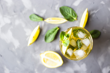 A glass glass with a cold tea with ice, mint and lemon on a gray concrete background. Summer cooling drink. Top view, flat layの写真素材