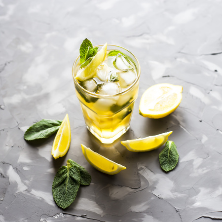 A glass glass with a cold tea with ice, mint and lemon on a gray concrete background. Summer cooling drinkの写真素材