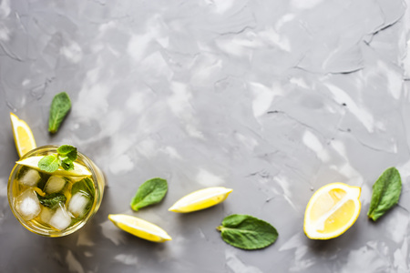 A glass glass with a cold tea with ice, mint and lemon on a gray concrete background. Summer cooling drink. Copyspace. Top view, flat layの写真素材