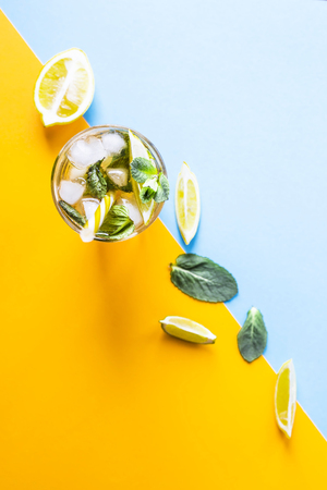 Ice tea with ice, lemon and mint on a combined colored yellow and blue background. Summer cold drink cocktail. Top view, flat layの写真素材
