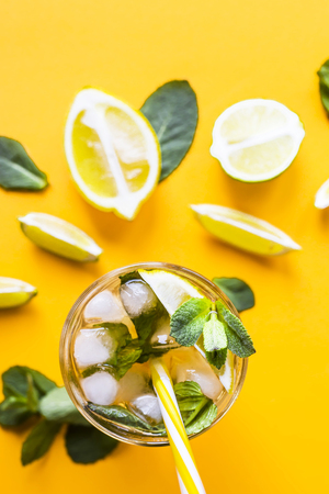 Ice tea with ice, lemon and mint on a combined colored yellow background. Summer cold drink cocktail. Top view, flat layの写真素材