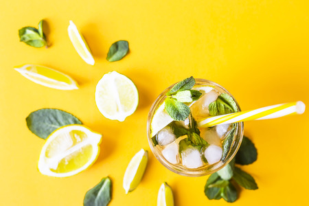 Ice tea with ice, lemon and mint on a combined colored yellow background. Summer cold drink cocktail. Top view, flat layの写真素材
