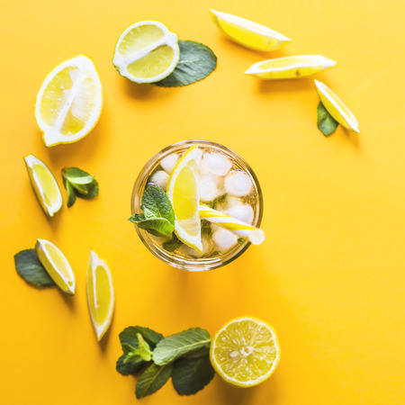 Ice tea with ice, lemon and mint on a combined colored yellow background. Summer cold drink cocktail. Top view, flat layの写真素材