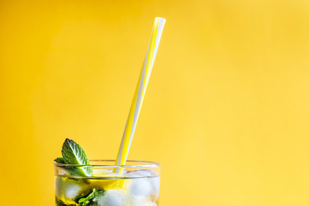 Ice tea with ice, lemon and mint on a combined colored yellow background. Summer cold drink cocktail. Copyspaceの写真素材