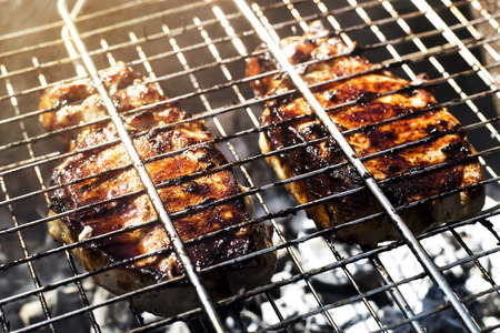 Two pork steaks on the grid are prepared on the grill outdoor. Summer family barbecue conceptの写真素材