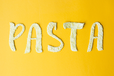 The word pasta is laid out in voluminous letters from small raw macaroni on a yellow background. Food on a bright backgroundの写真素材