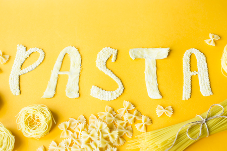 The word pasta is laid out in bulk letters from small raw macaroni on a yellow background next to a variety of kinds of pasta. Food on a bright backgroundの写真素材