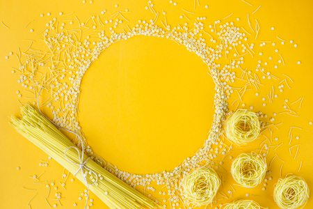 Empty circle among different types of raw macaroni on a bright yellow background. Copyspaceの写真素材