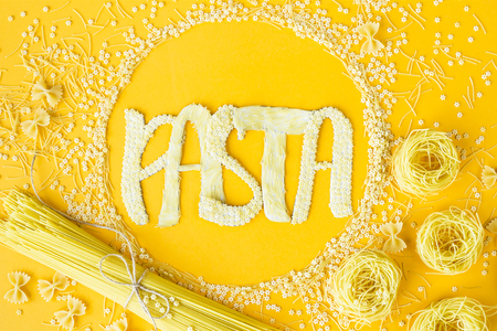 The word pasta is laid out in voluminous letters from small raw macaroni in a circle among various types of pasta. Food on a bright backgroundの写真素材