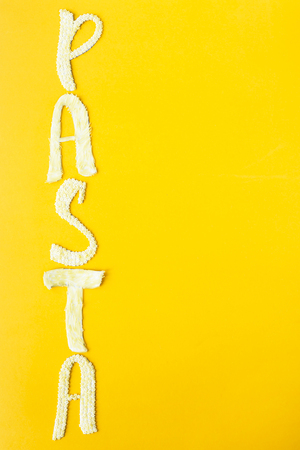 The word pasta is laid out in voluminous letters from small raw macaroni on a yellow background. Food on a bright backgroundの写真素材